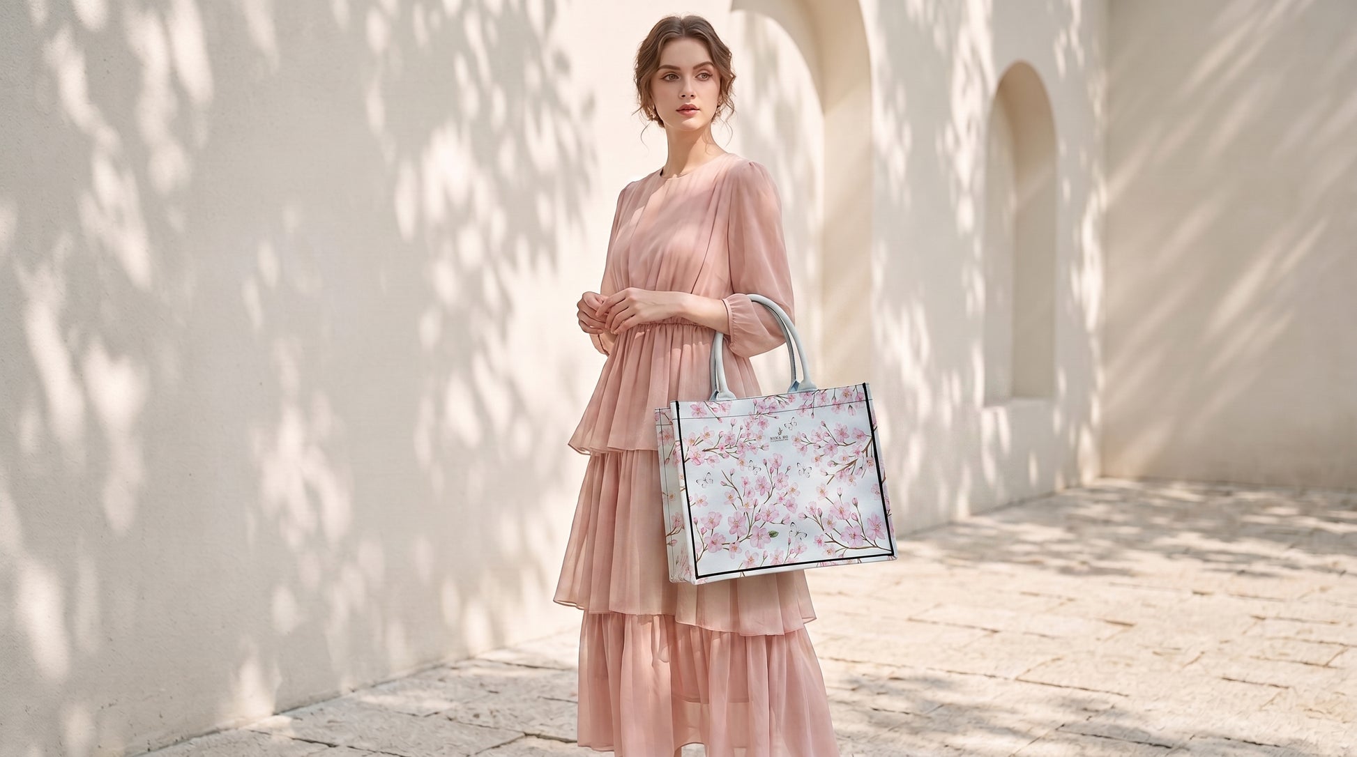 A sophisticated woman in a soft pink tiered dress holds a pale blue canvas tote adorned with delicate hand-painted cherry blossom motifs and fluttering white butterflies, embodying subtle artistry and refined femininity by NINA HO ILLUSTRATION.
