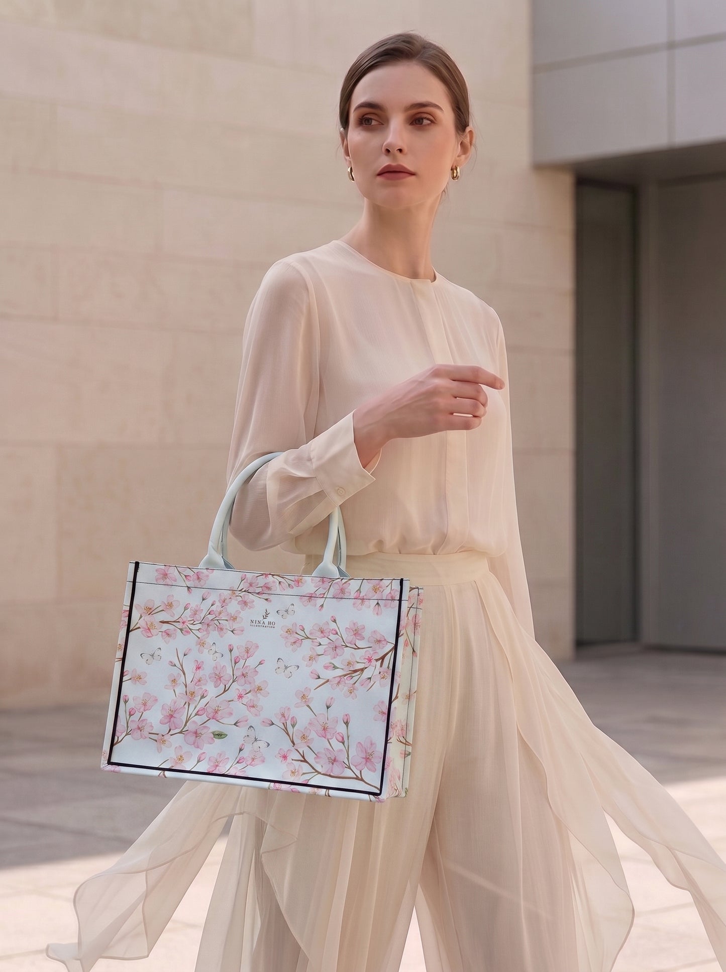 A refined tote bag from NINA HO ILLUSTRATION featuring delicate hand-painted cherry blossom motifs with Taiwanese white butterflies on a pale blue canvas, embodying subtle botanical elegance and Parisian-chic sophistication.