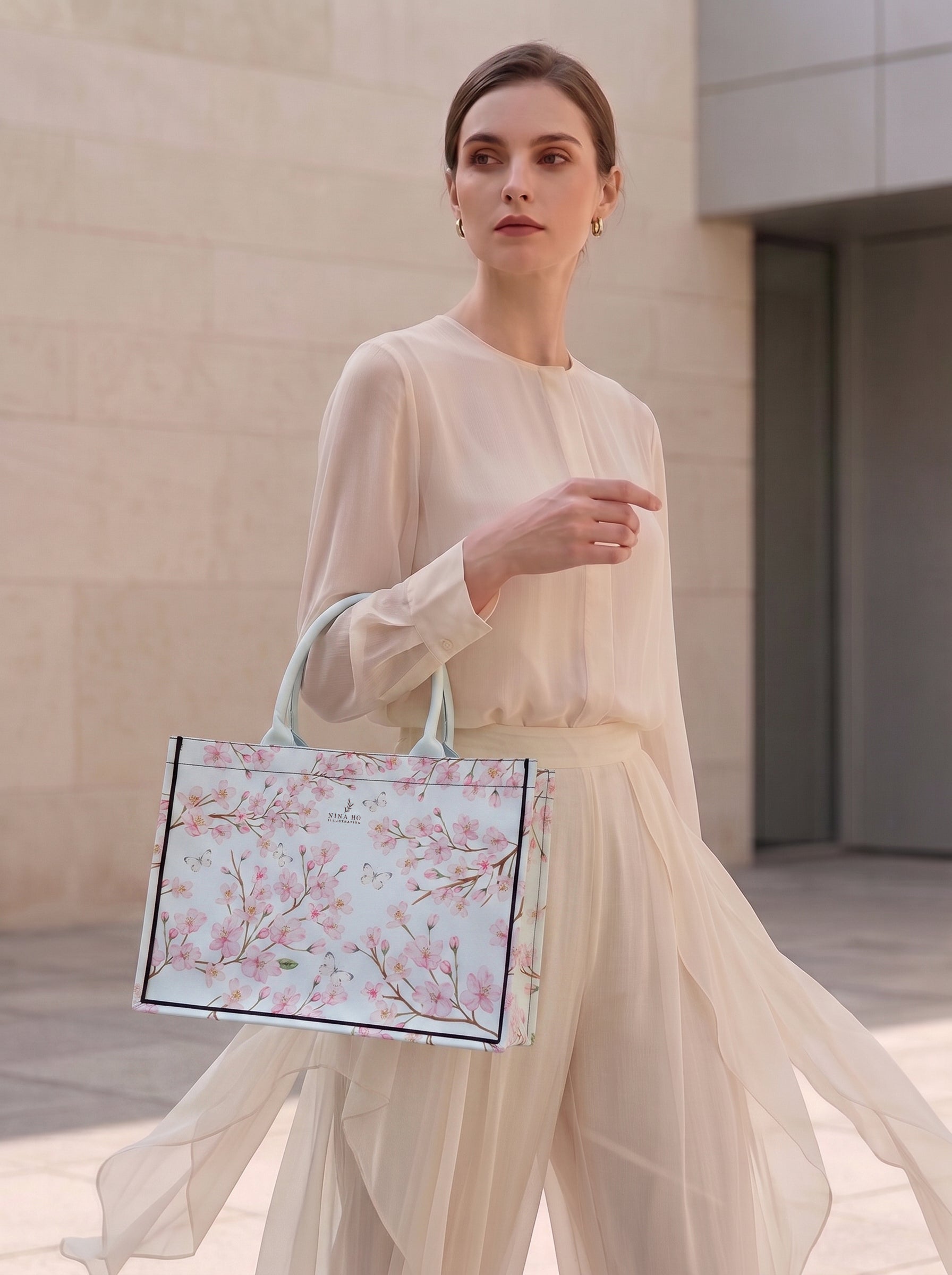 A refined tote bag from NINA HO ILLUSTRATION featuring delicate hand-painted cherry blossom motifs with Taiwanese white butterflies on a pale blue canvas, embodying subtle botanical elegance and Parisian-chic sophistication.