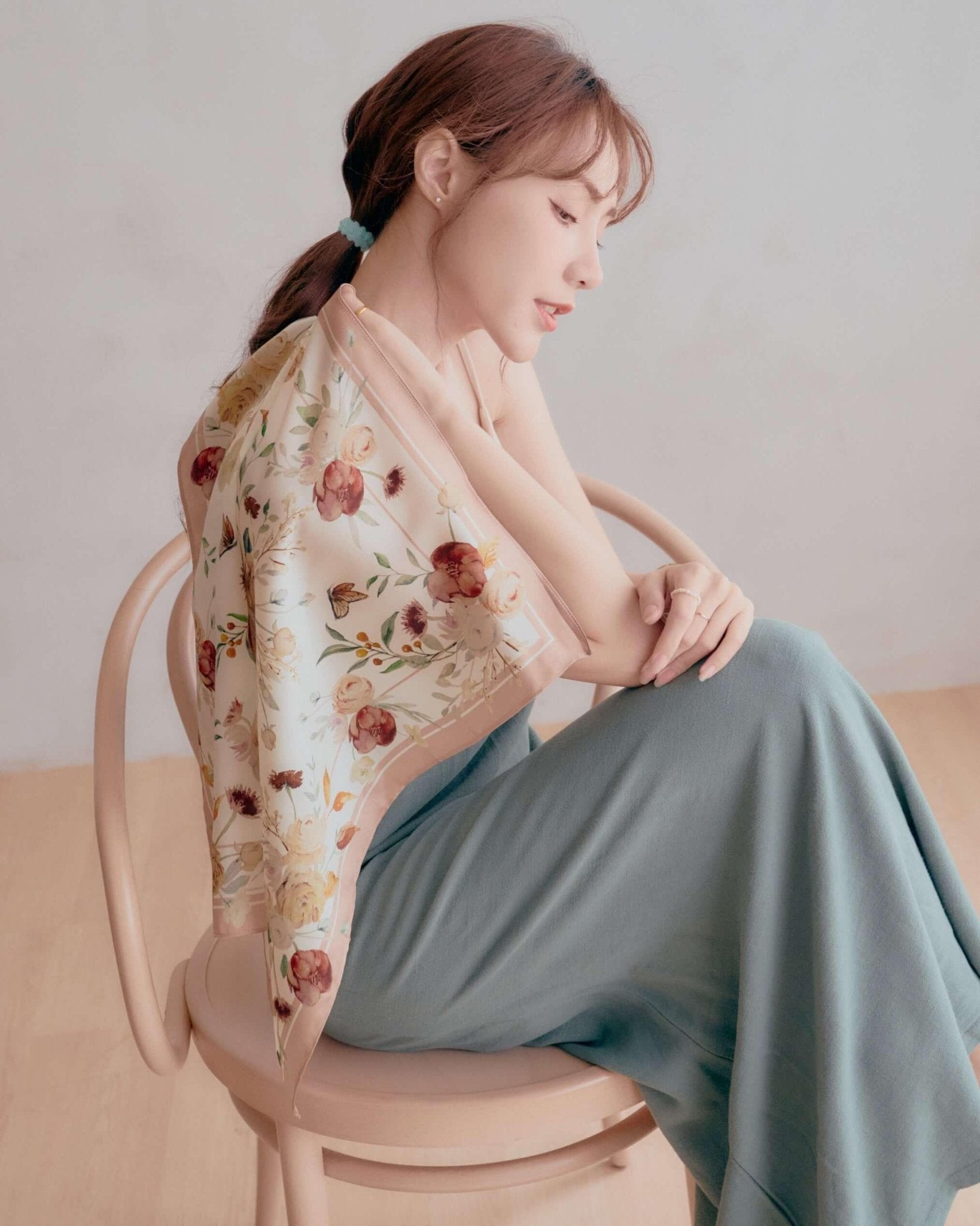 A delicate 100% mulberry silk scarf with hand-painted rose and  crimson tulip bouquet, draped elegantly on a seated woman.